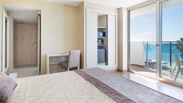 Un dormitorio con cama, escritorio y silla. Posee una puerta corredera que da a un balcón con vistas al océano.