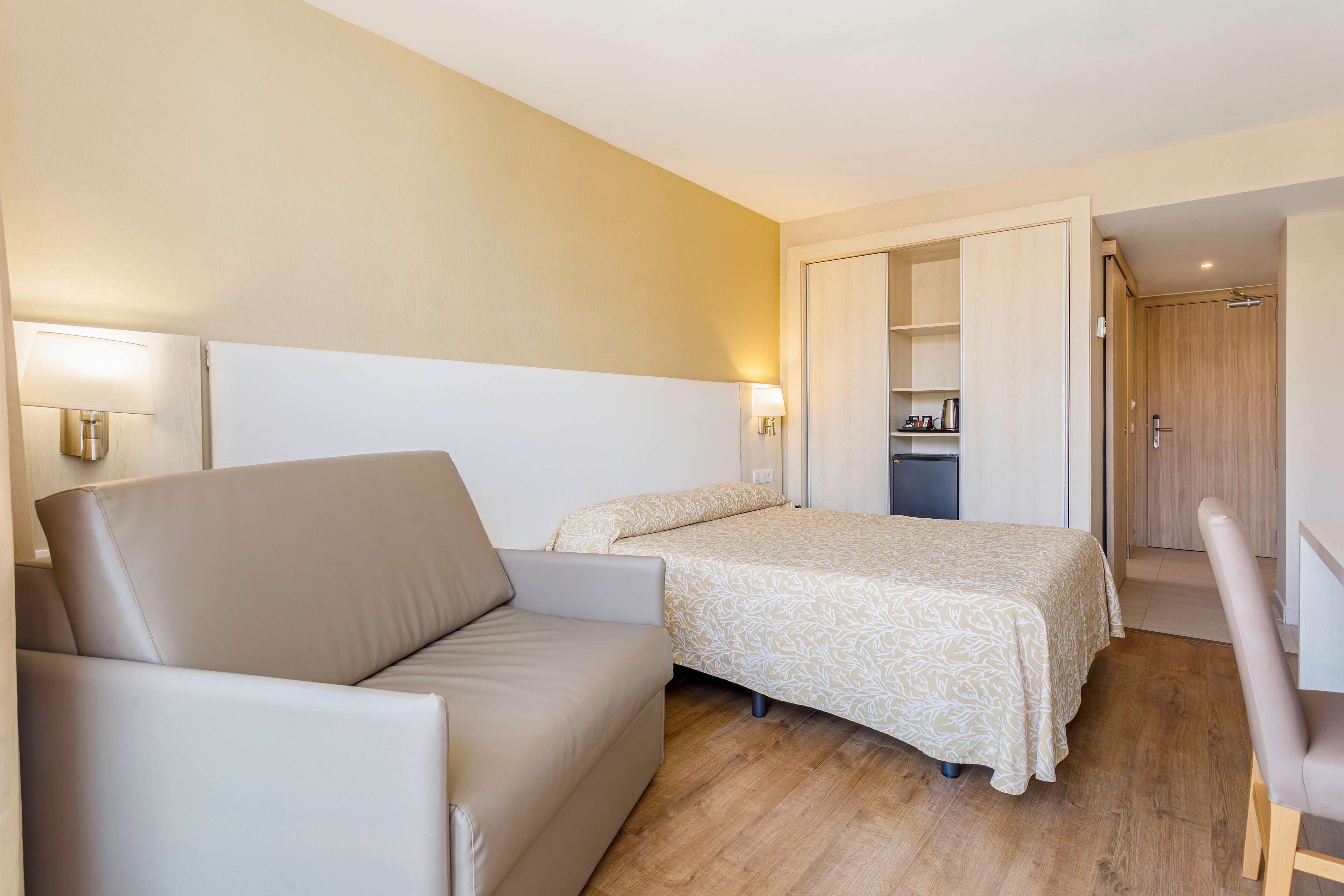 A hotel room with a bed, a sofa, a desk, and a wardrobe.