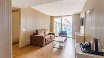 Una habitación de hotel moderna con piso de madera, un sofá marrón, una pequeña mesa de centro y un escritorio con una tetera y bandeja.