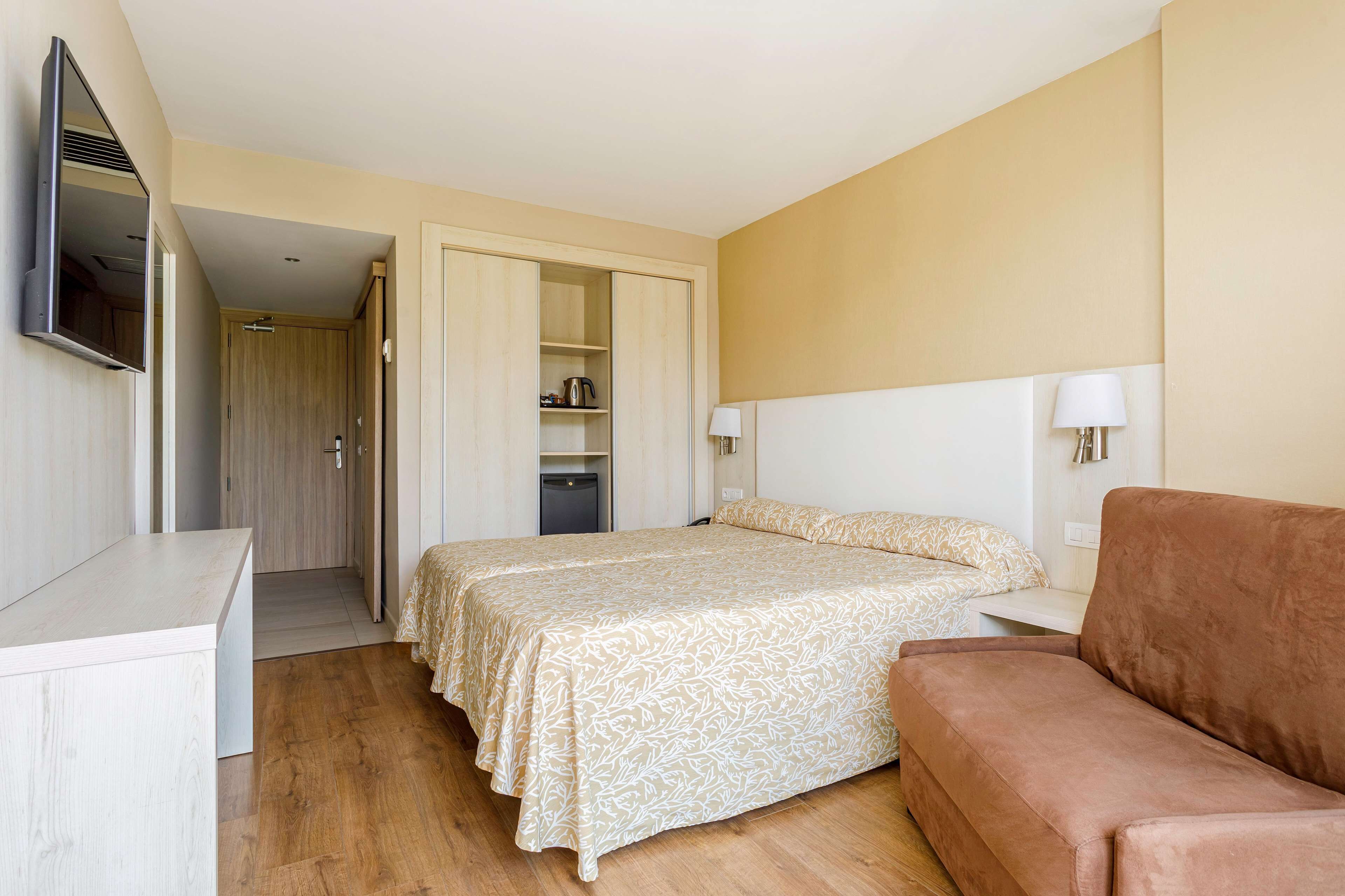 A hotel room with a bed, a sofa, a desk, a TV, and a wardrobe.