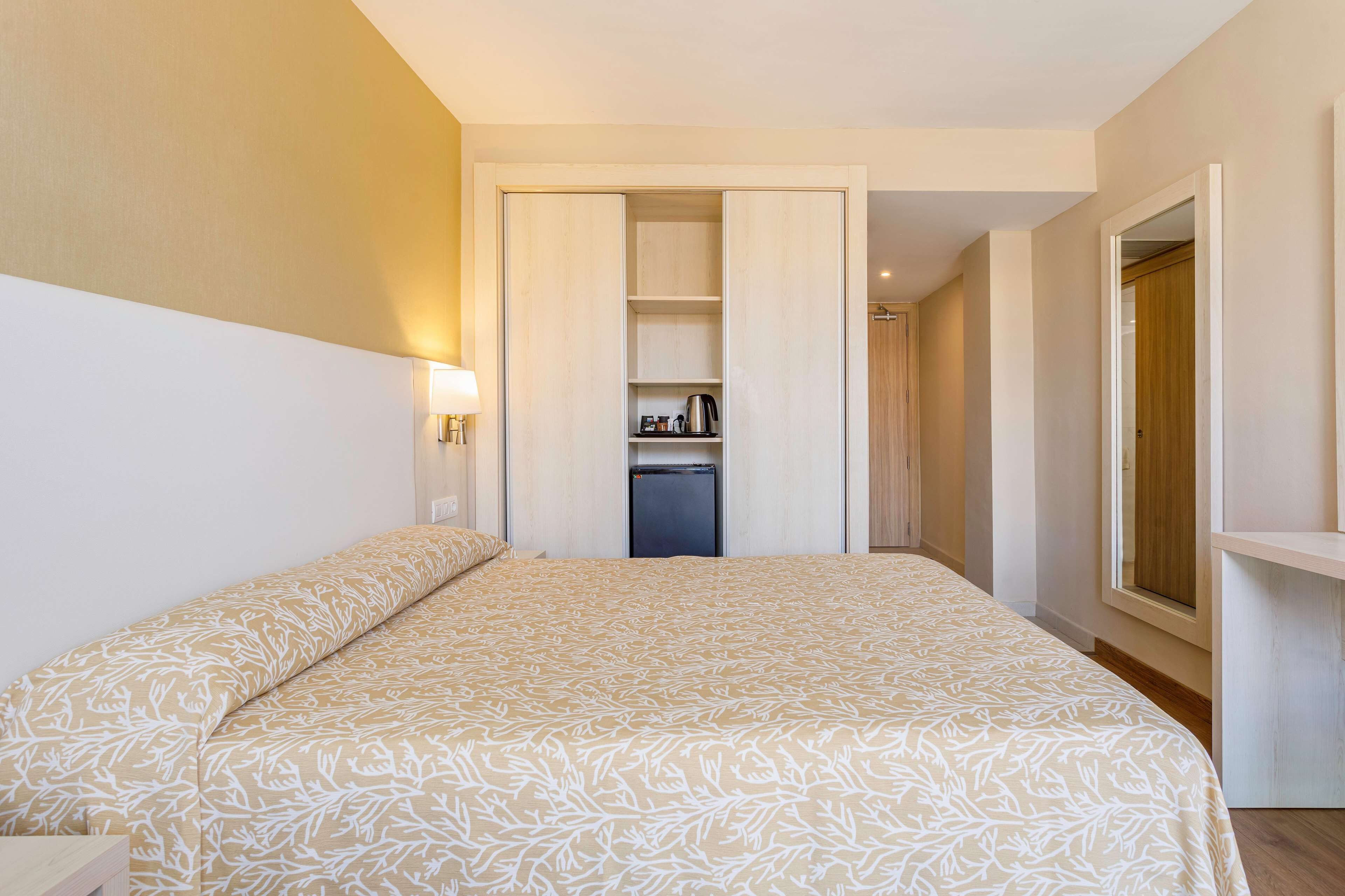 A bedroom with a bed, a wardrobe, a small kitchenette, and a window.