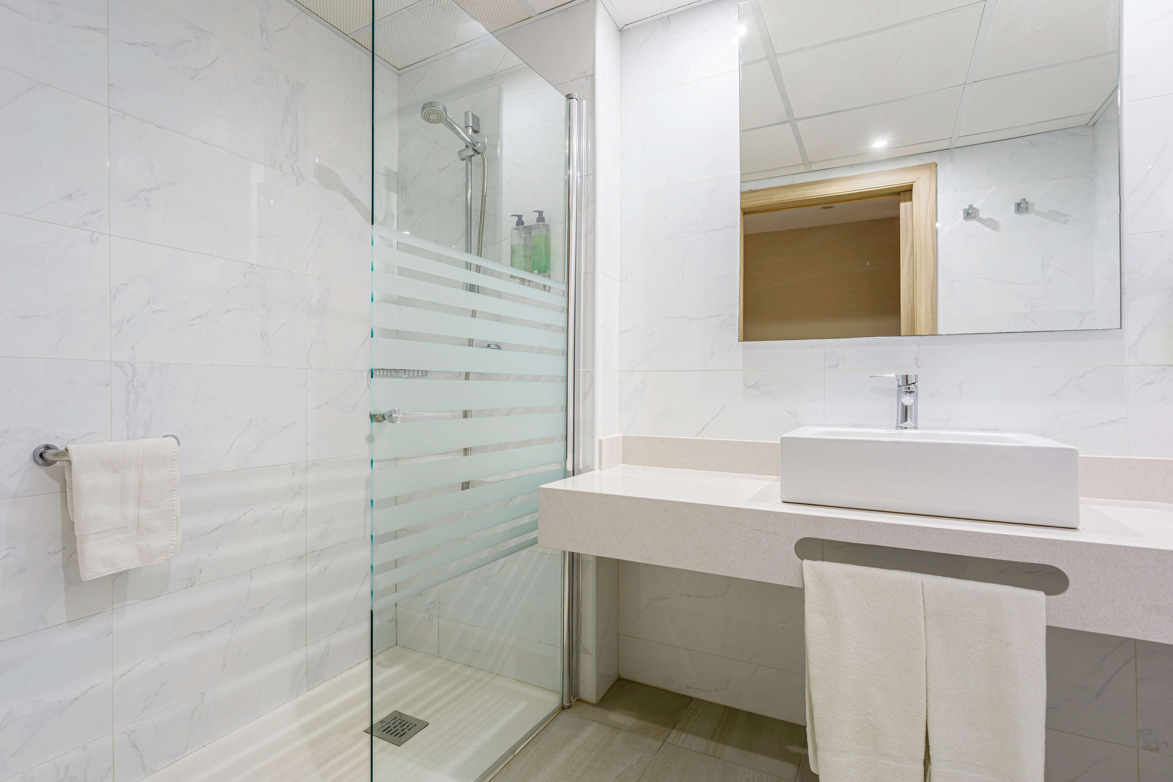 Un bagno moderno con box doccia in vetro, un lavandino bianco e uno specchio grande.