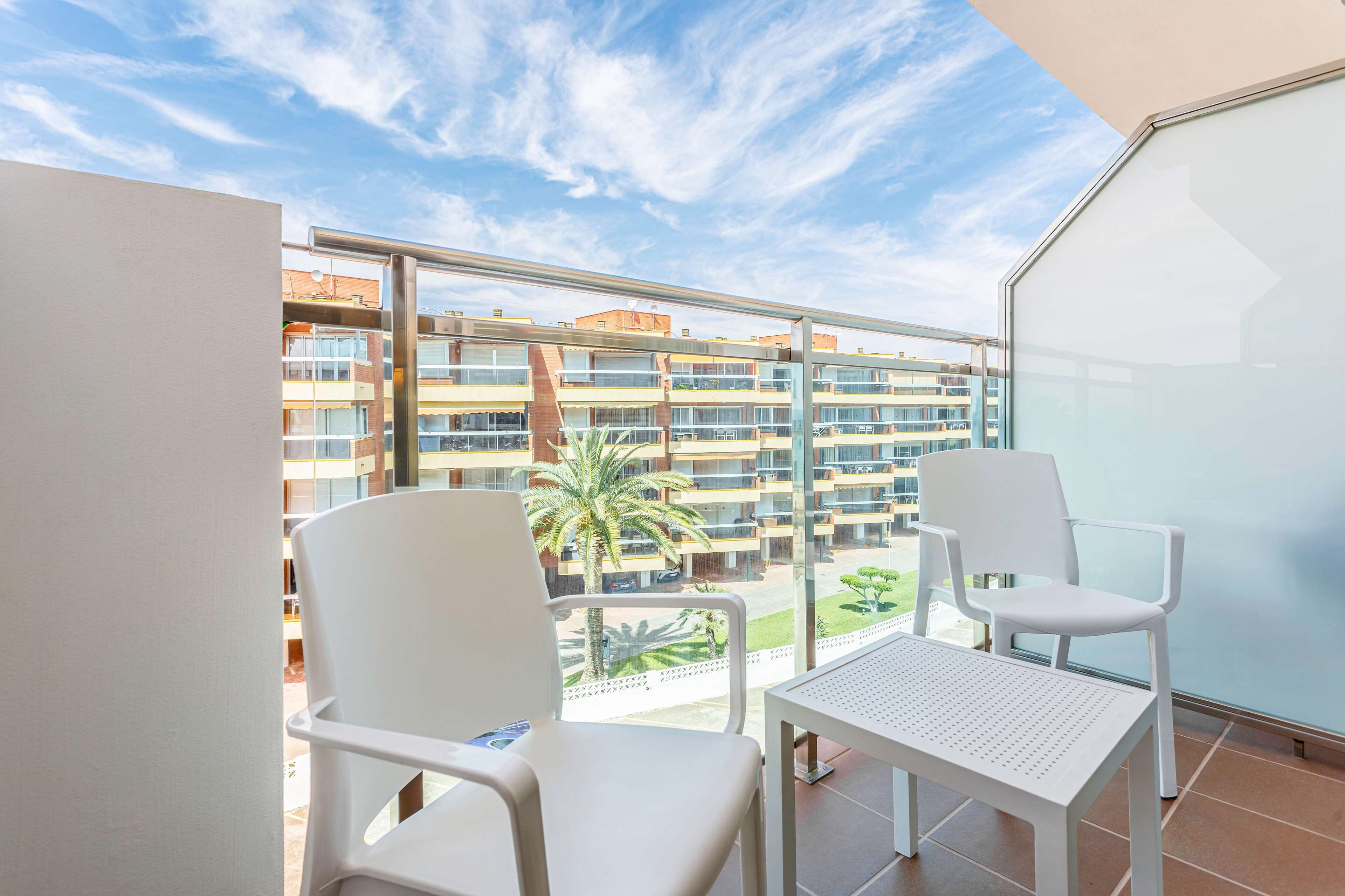 A balcony with two white chairs and a small table, overlooking a residential area with multiple apartment buildings.