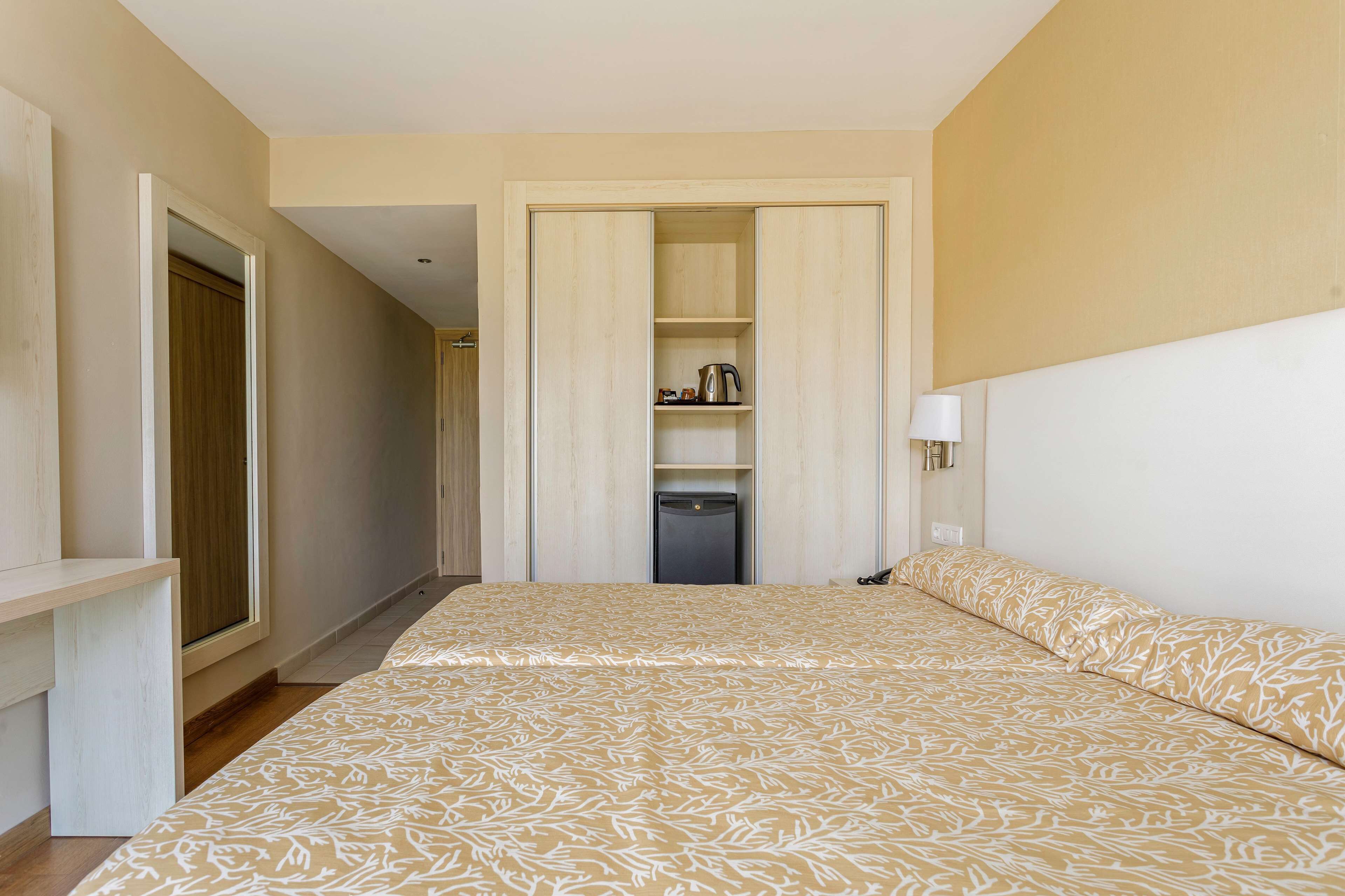 A hotel room with a bed, a wardrobe, a small table, and a nightstand.