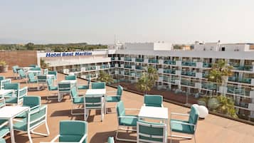 Een terras op het dak met zitplaatsen buiten en uitzicht op het hotelinterieur.