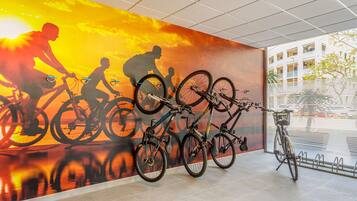 Um mural na parede com ciclistas, um suporte para bicicletas e vista de um edifício.