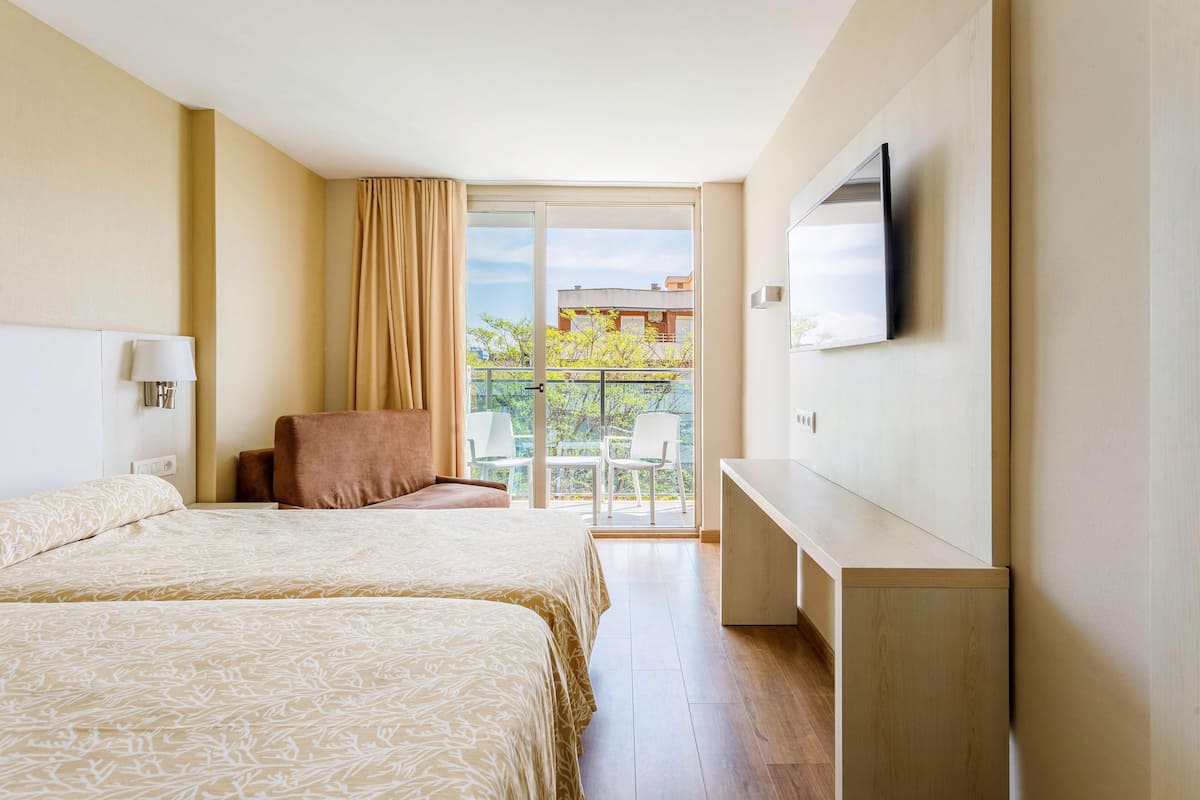 A hotel room with two beds, a TV, a desk, and a balcony with a view of the outside.
