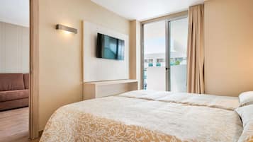 Habitación de hotel con una cama grande, un televisor de pantalla plana montado en la pared y una puerta corrediza de vidrio que da a un balcón.