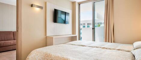 A hotel room with a large bed, a flat-screen TV mounted on the wall, and a sliding glass door leading to a balcony.
