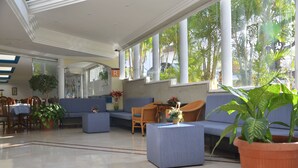 Un vestíbulo amplio con zona de estar, mostrador de recepción y grandes ventanales con vistas al exterior.