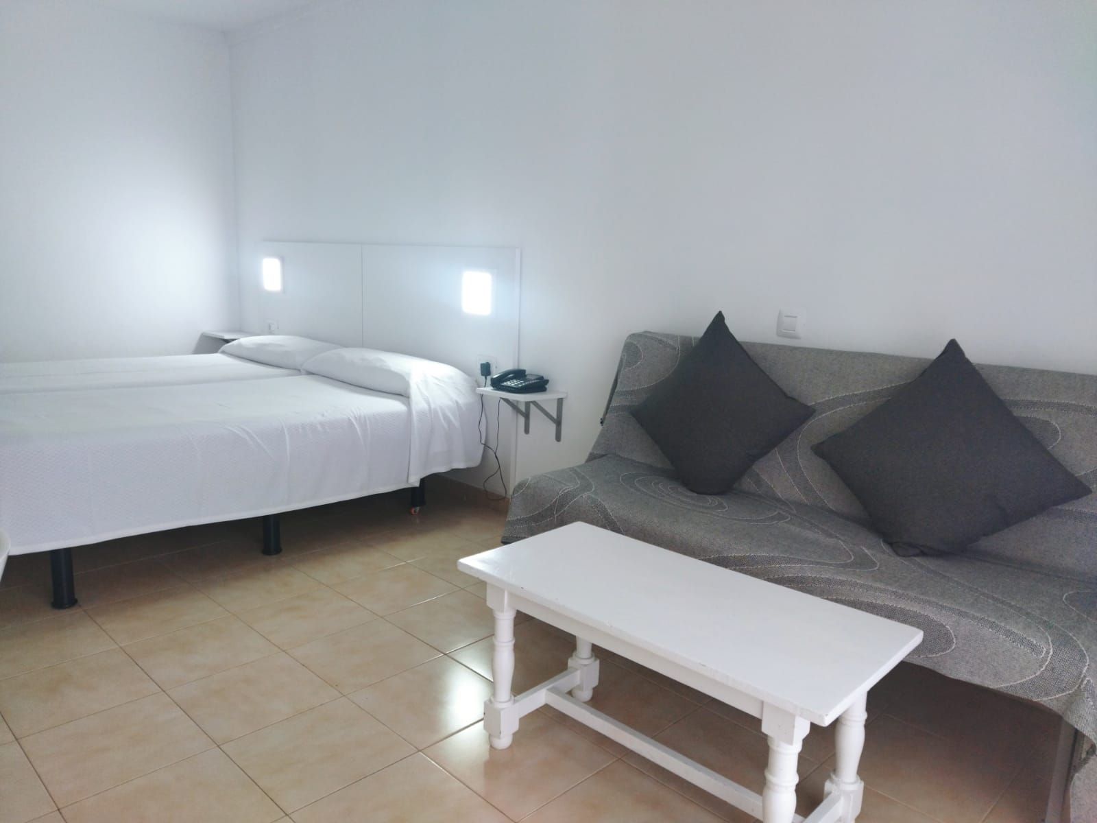 Ein Zimmer mit einem Bett, einem weißen Tisch und einer Couch mit Kissen.