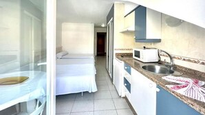 Habitación de hotel compacta con kitchenette, una cama y un vidrio que da a un balcón.