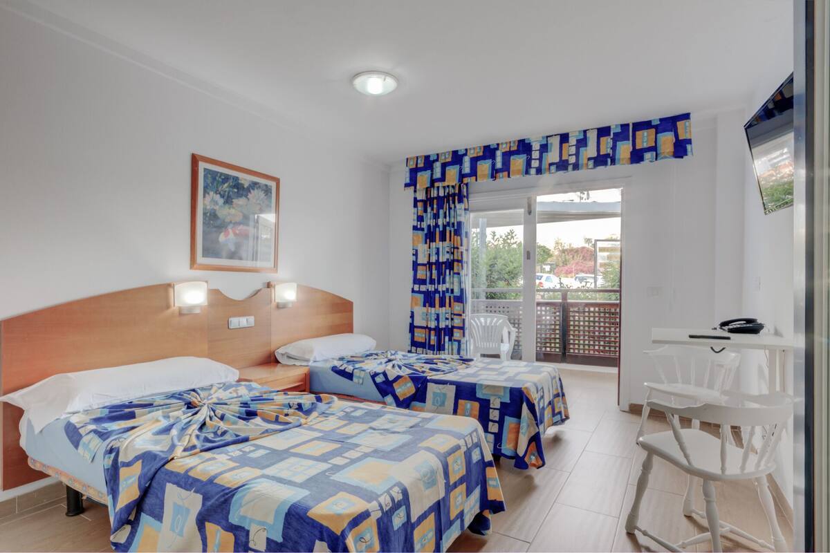 Une chambre d’hôtel avec deux lits, un balcon, un bureau et une chaise.