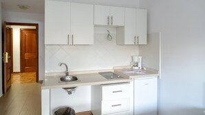 Una cocina compacta con armarios blancos, un lavamanos de acero inoxidable y un lavavajillas empotrado.
