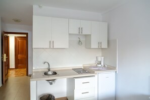 Een kleine keuken met witte kasten, een roestvrijstalen spoelbak en een ingebouwde vaatwasser.