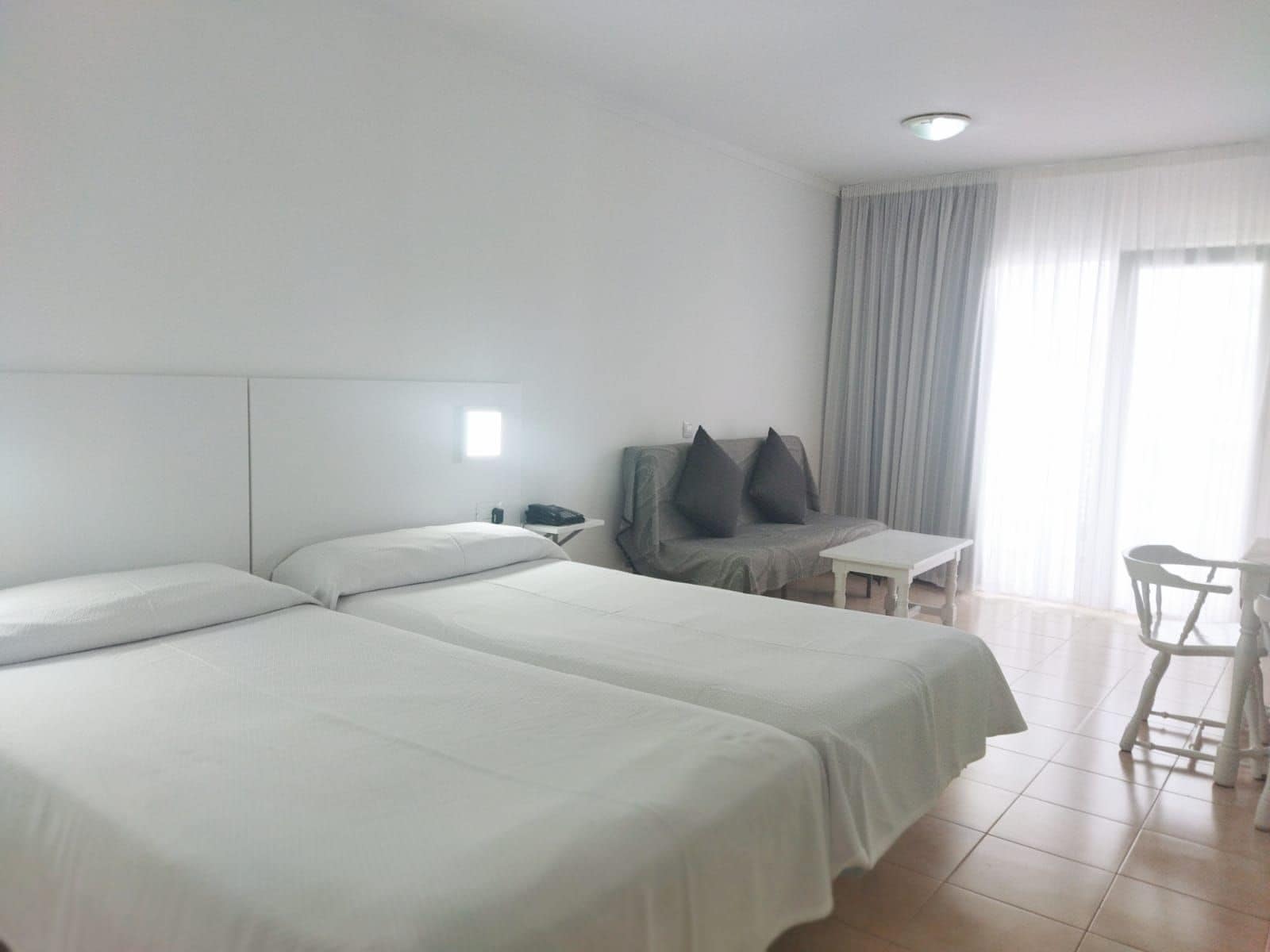Habitación de hotel con dos camas, una mesita, un sofá y una ventana con cortinas.