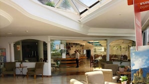 A spacious lobby with high ceilings, a glass ceiling, and a seating area with chairs and tables. - Pez Azul (Puerto de la Cruz)