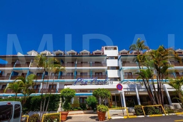 Een hotel met meerdere verdiepingen, balkons, palmbomen en een helderblauwe lucht.