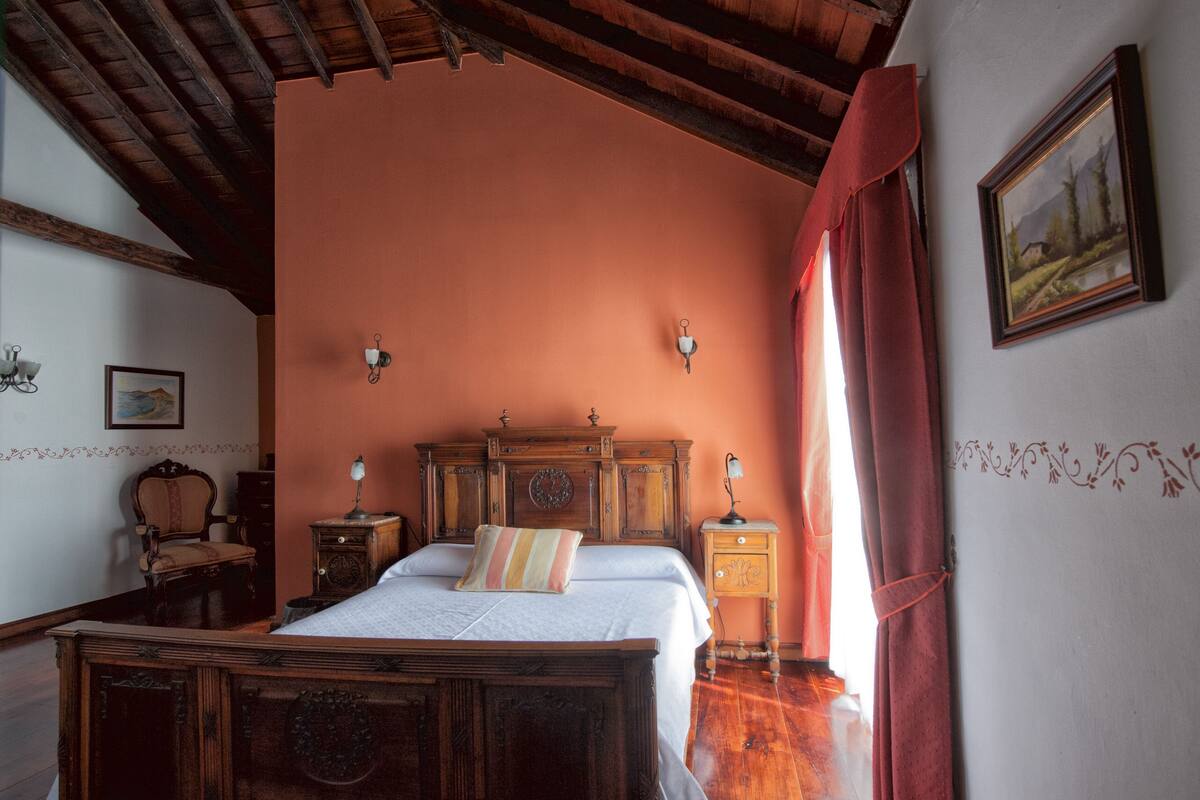 Une chambre à coucher avec un lit en bois, deux tables de chevet, une chaise et un tableau accroché au mur.