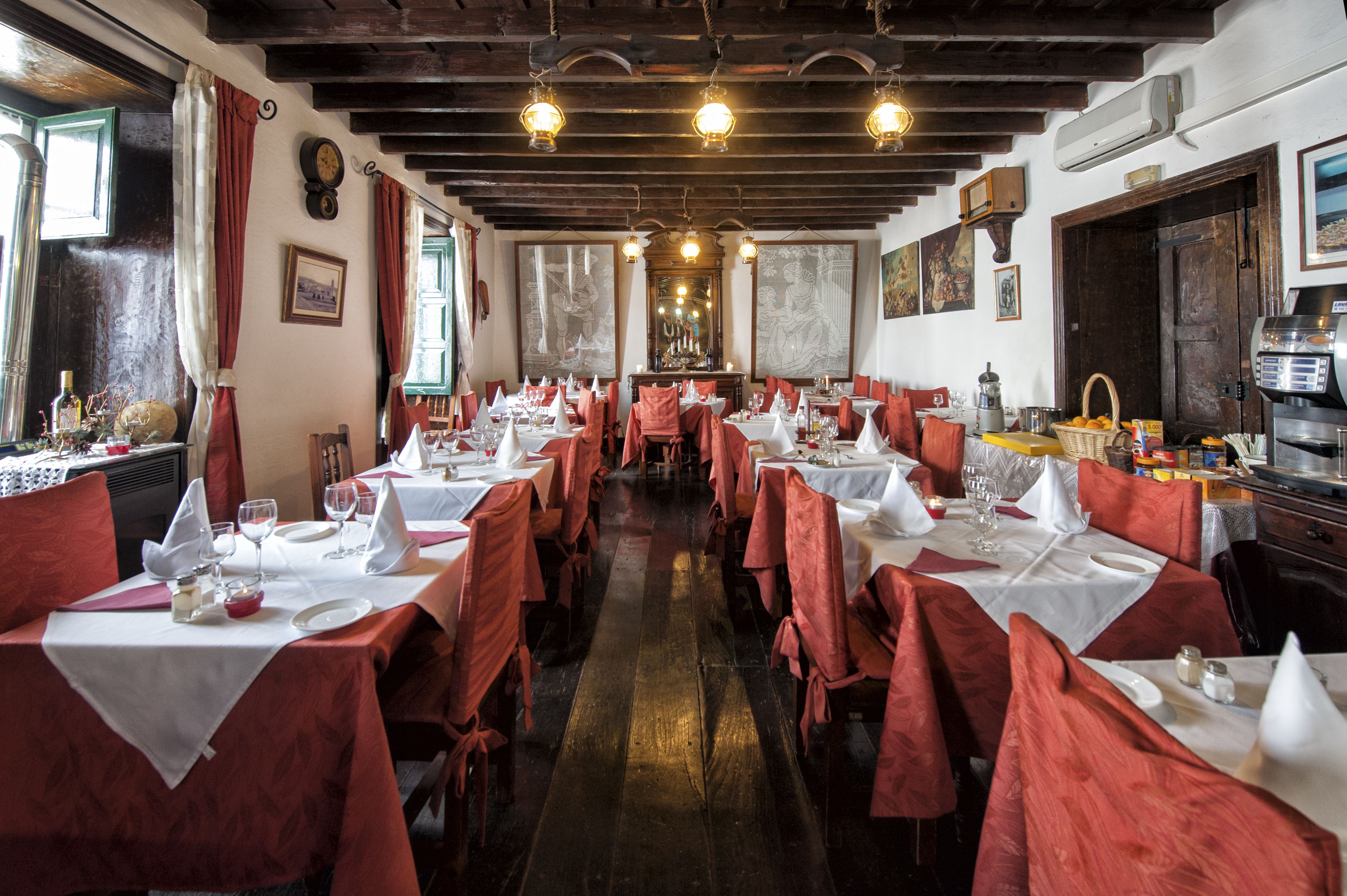 Un ristorante con diversi tavoli apparecchiati, travi in legno al soffitto e opere d'arte alle pareti.