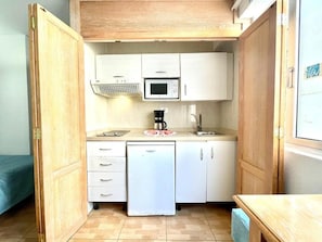 A compact kitchen with white cabinets, a microwave, a coffee maker, and a small refrigerator.