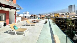 Una terraza en la azotea con sillones de descanso, barandilla de cristal y vistas a la ciudad.