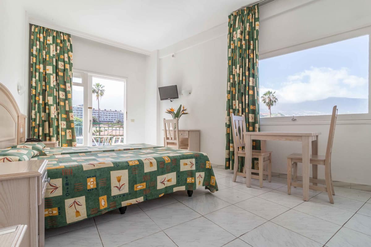 Habitación de hotel con cama, escritorio, silla, televisor y balcón con vistas.