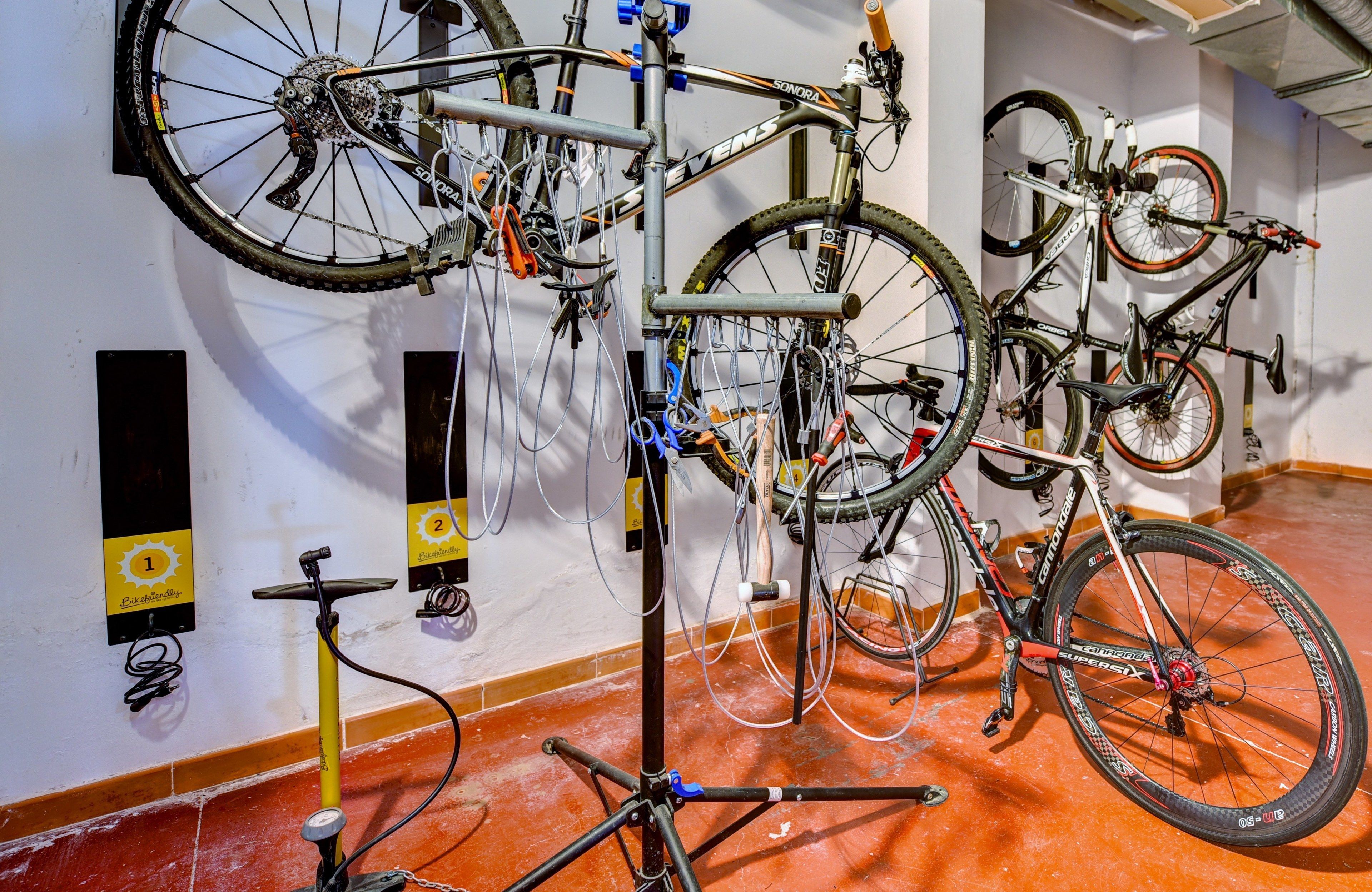 Bicycles mounted on a wall with numbered hooks, a tripod stand, and a bicycle repair stand.