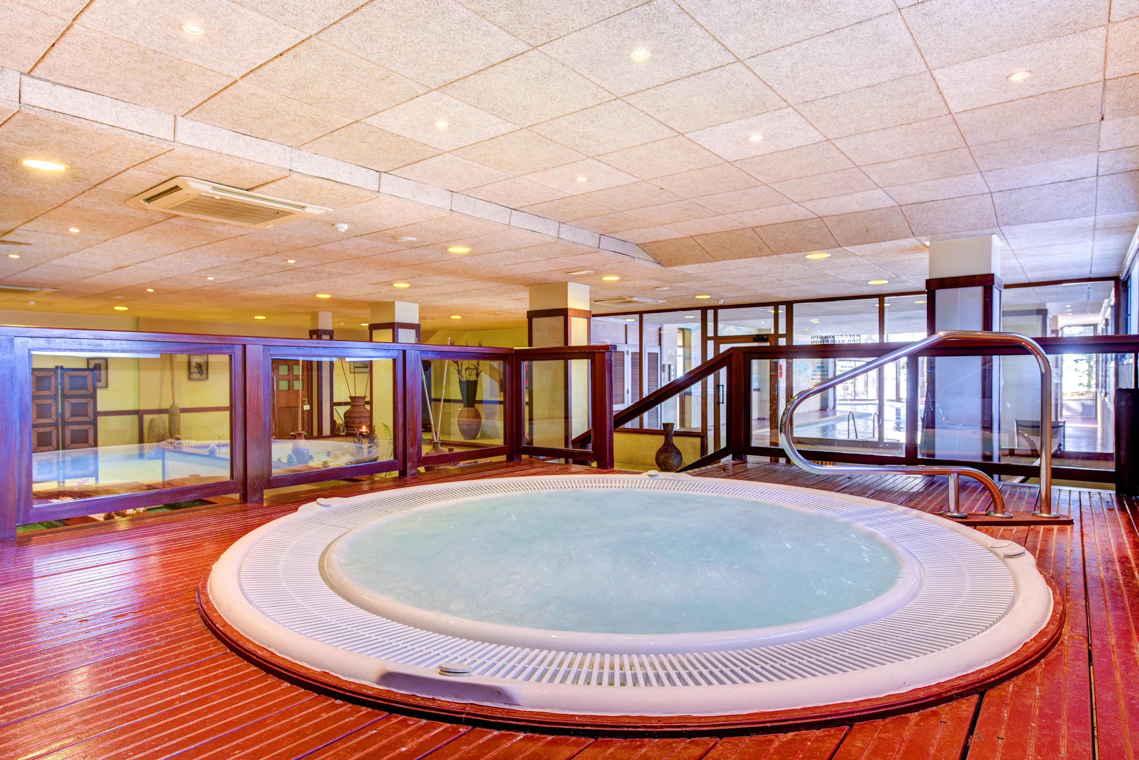 Un jacuzzi en una habitación con suelo de madera, paredes de vidrio y una escalera.