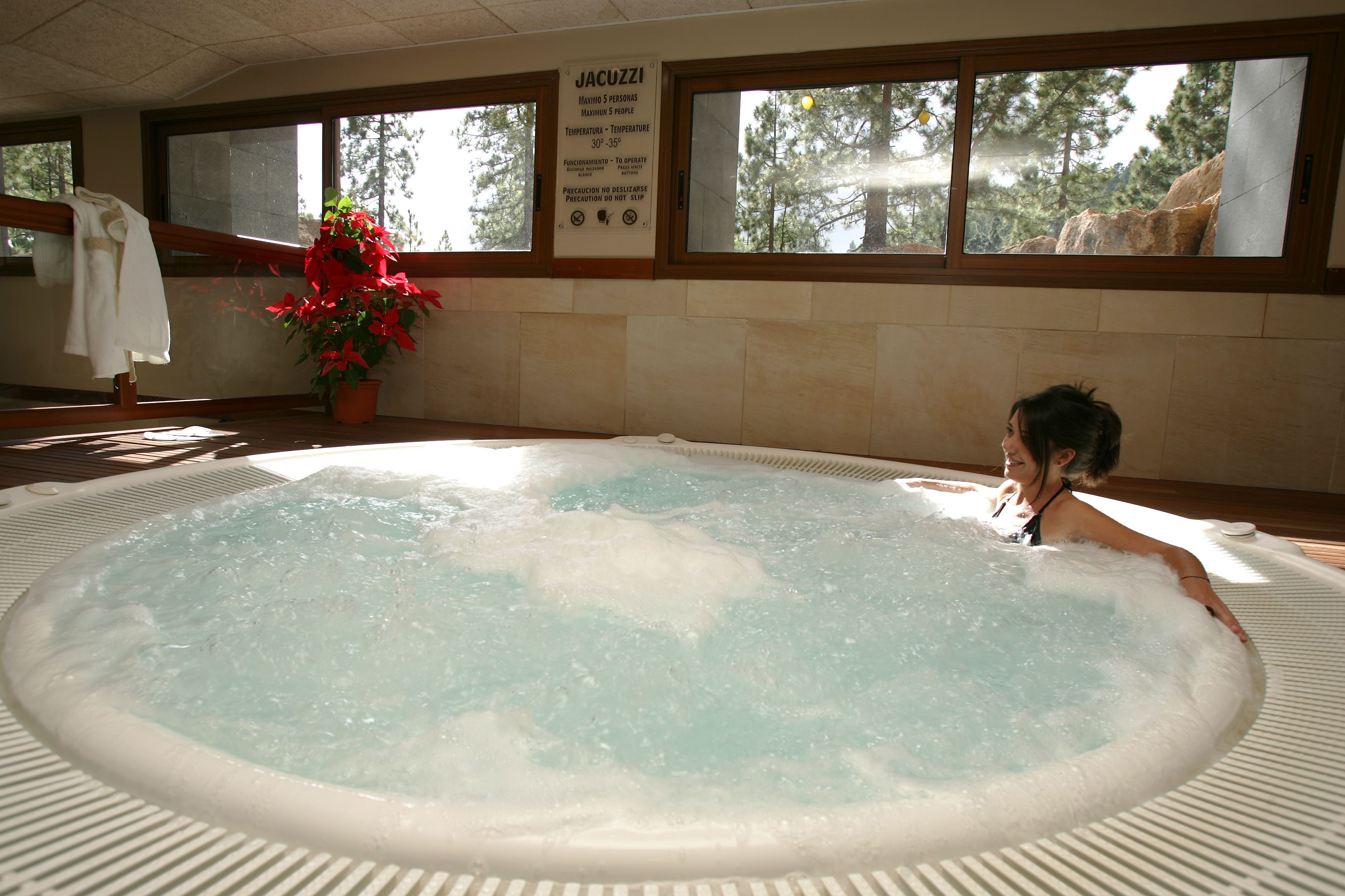 A hot tub with a person relaxing in it, a potted plant, and a sign with temperature guidelines.