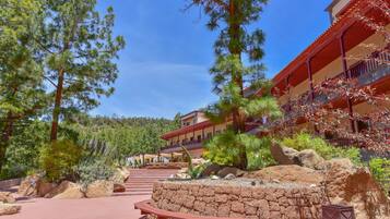 A resort with a stone pathway leading to a building with red and beige exterior walls, surrounded by pine trees and a mountainous backdrop.