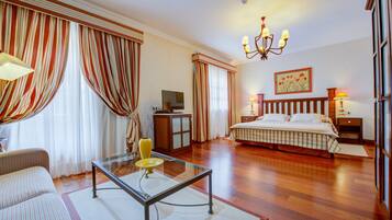 Una habitación de hotel con una cama, televisión, mesa de vidrio, sofá y cortinas.