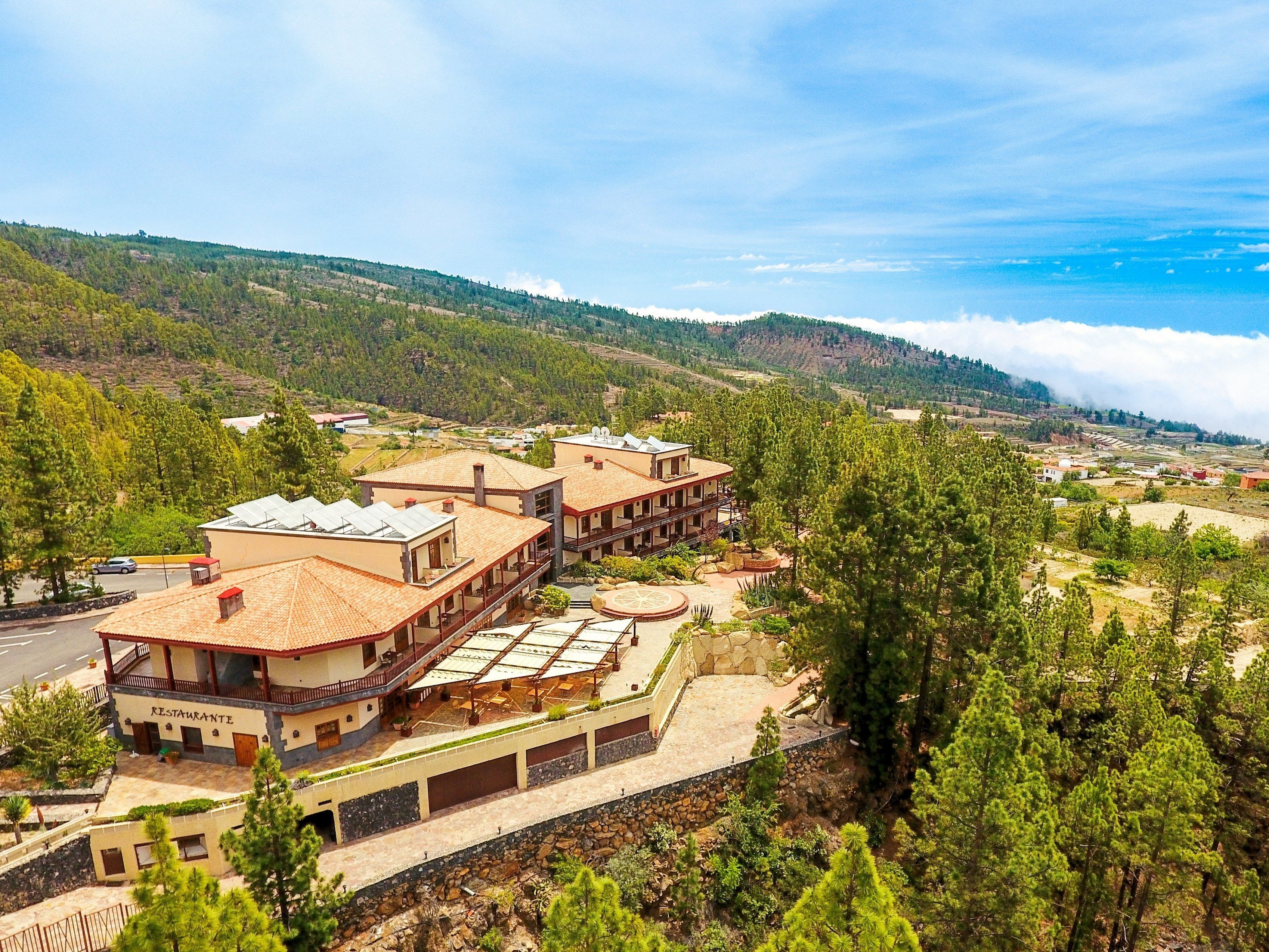 A hotel with multiple buildings, including a restaurant, set against a mountainous backdrop with pine trees and a clear sky.