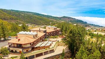 A hotel with multiple buildings, including a restaurant, set against a mountainous backdrop with pine trees and a clear sky.