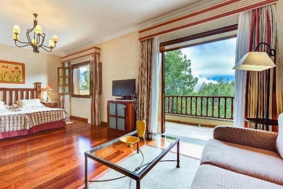 A hotel room with a bed, a sofa, a TV, and a balcony with a view.