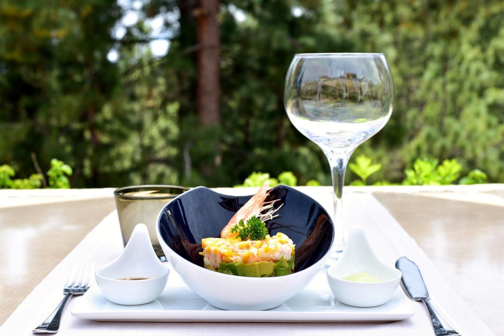 Una mesa de comedor con un plato de mariscos, una copa de vino blanco y recipientes pequeños con salsas.