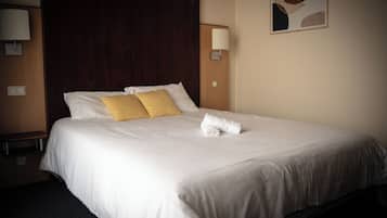 A hotel room with a large bed, a wooden headboard, a wall-mounted lamp, and a framed artwork.