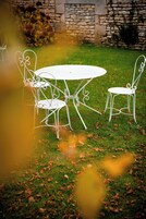 Conjunto de mesa e cadeiras de metal branco sobre um gramado com um muro de pedra ao fundo.