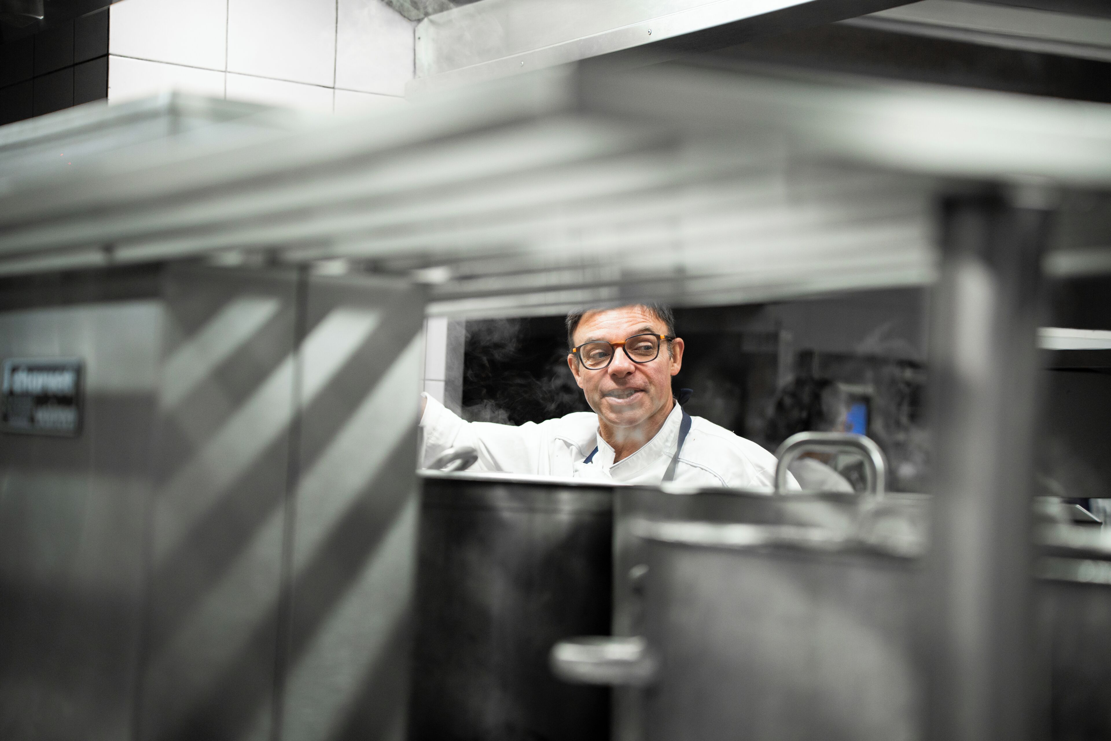Una persona con camisa blanca de pie en una cocina con electrodomésticos de acero inoxidable y un extractor de humos visible.