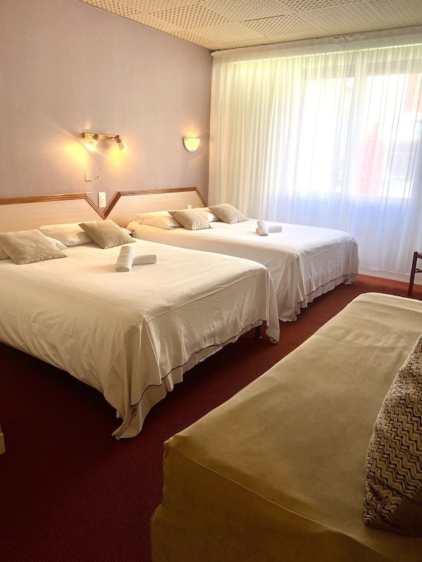 A hotel room with two beds, a wooden headboard, and a large window with sheer curtains.