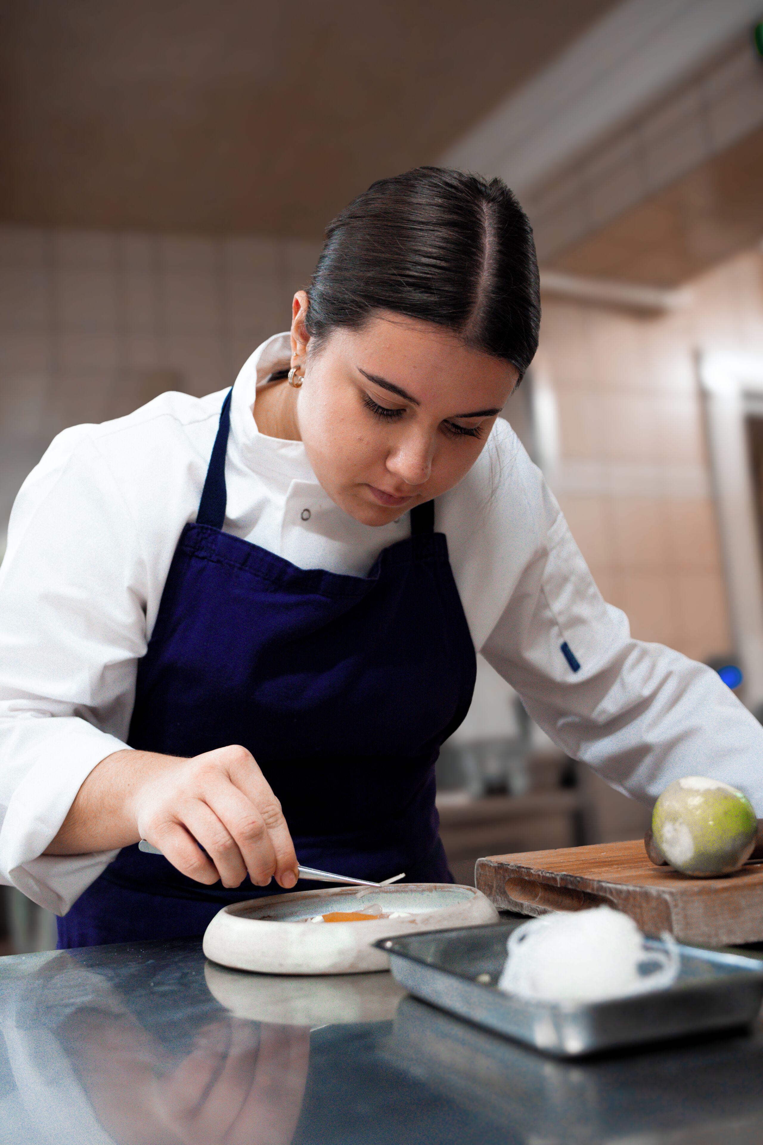 A person in a white shirt and dark apron preparing food on a kitchen counter.