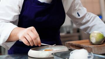 A person in a white shirt and dark apron preparing food on a kitchen counter.