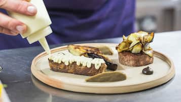 A person in a purple apron pouring a white substance onto food items on a plate.