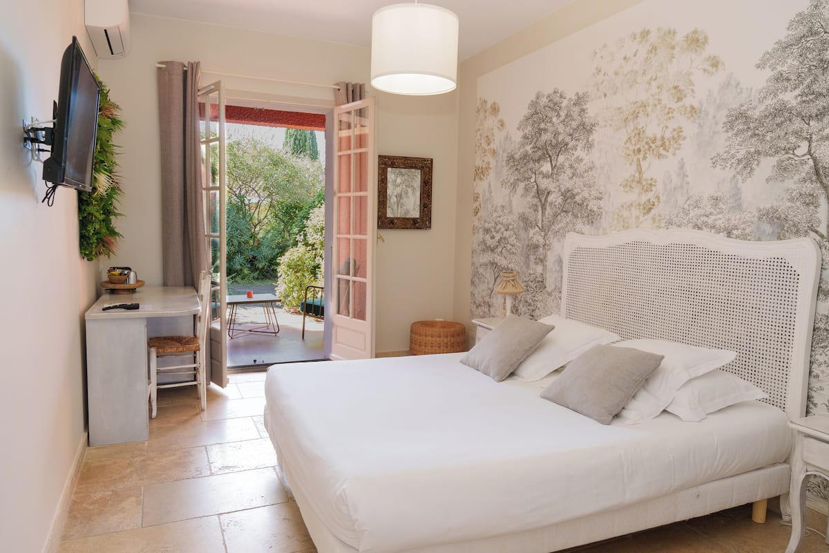 A bedroom with a bed, a desk, and a chair, a television, and a door leading to an outdoor area.