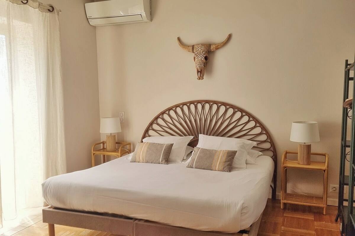 A bedroom with a wooden bed, two bedside tables with lamps, a wall-mounted air conditioner, and a decorative bull head.