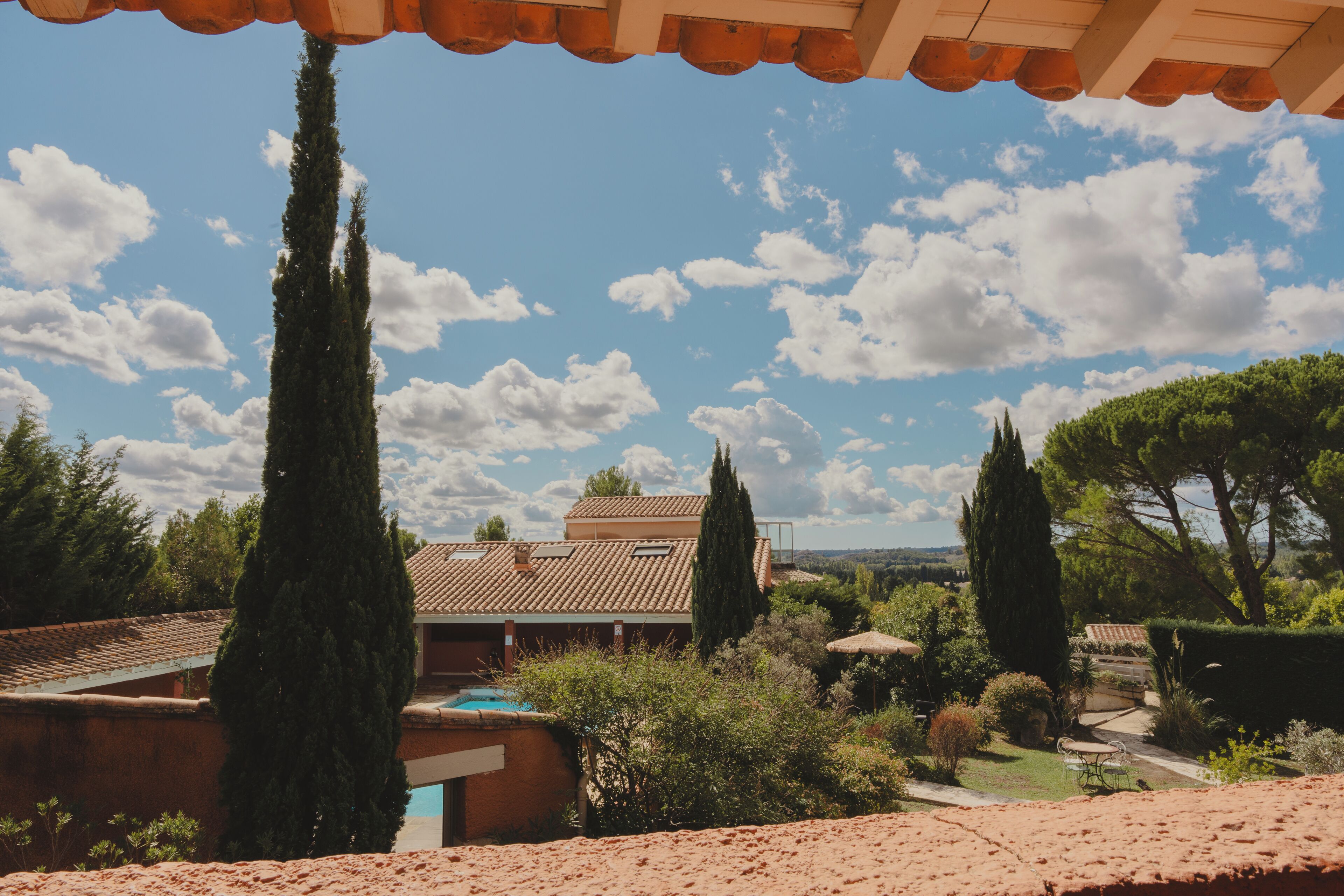A house with a tiled roof, a swimming pool, and surrounding greenery.