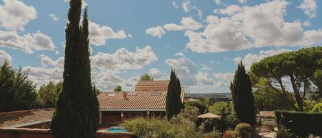 A house with a tiled roof, a swimming pool, and surrounding greenery.