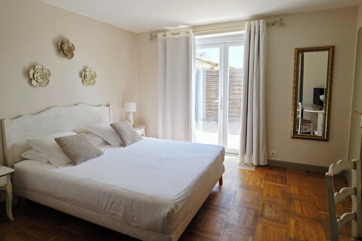 A bedroom with a large bed, a nightstand, a desk with a chair, a mirror, and a sliding glass door leading to an outdoor area.