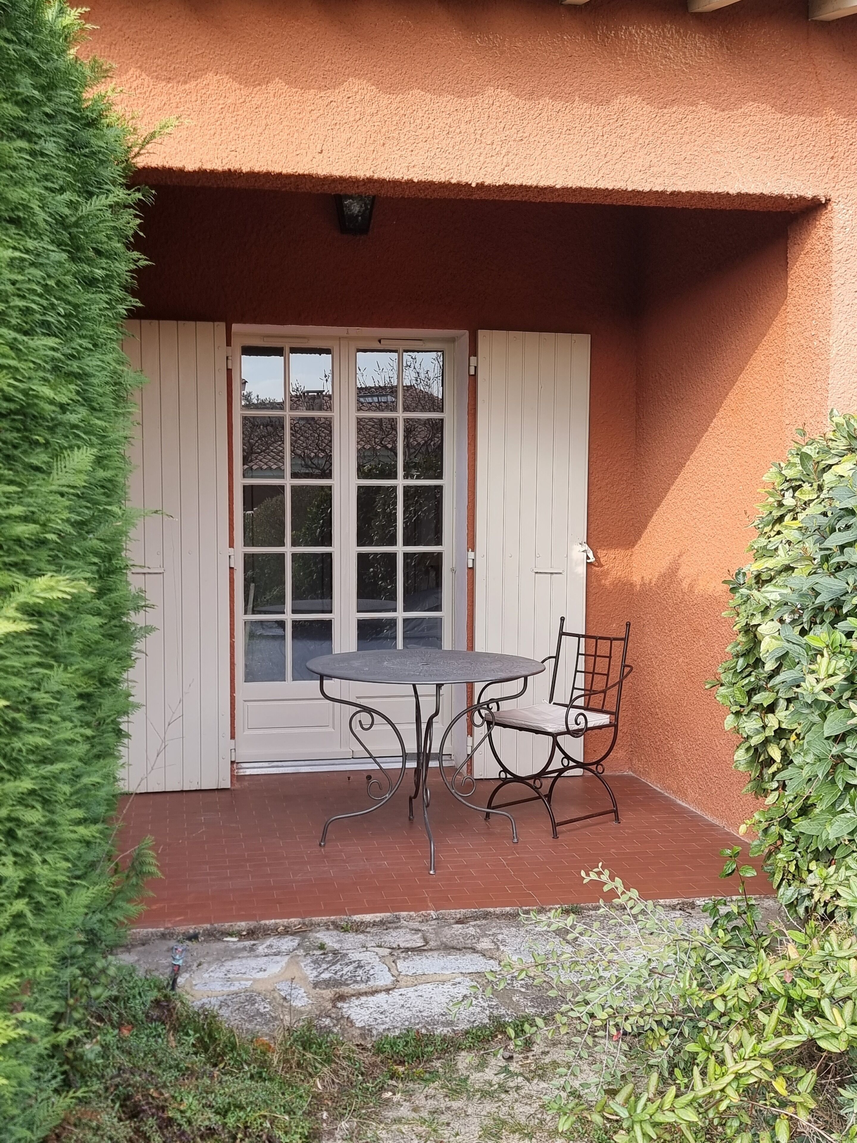 Eine Terrasse mit Tisch und Stuhl, eine Tür mit Glasfeldern und eine Ziegelwand.
