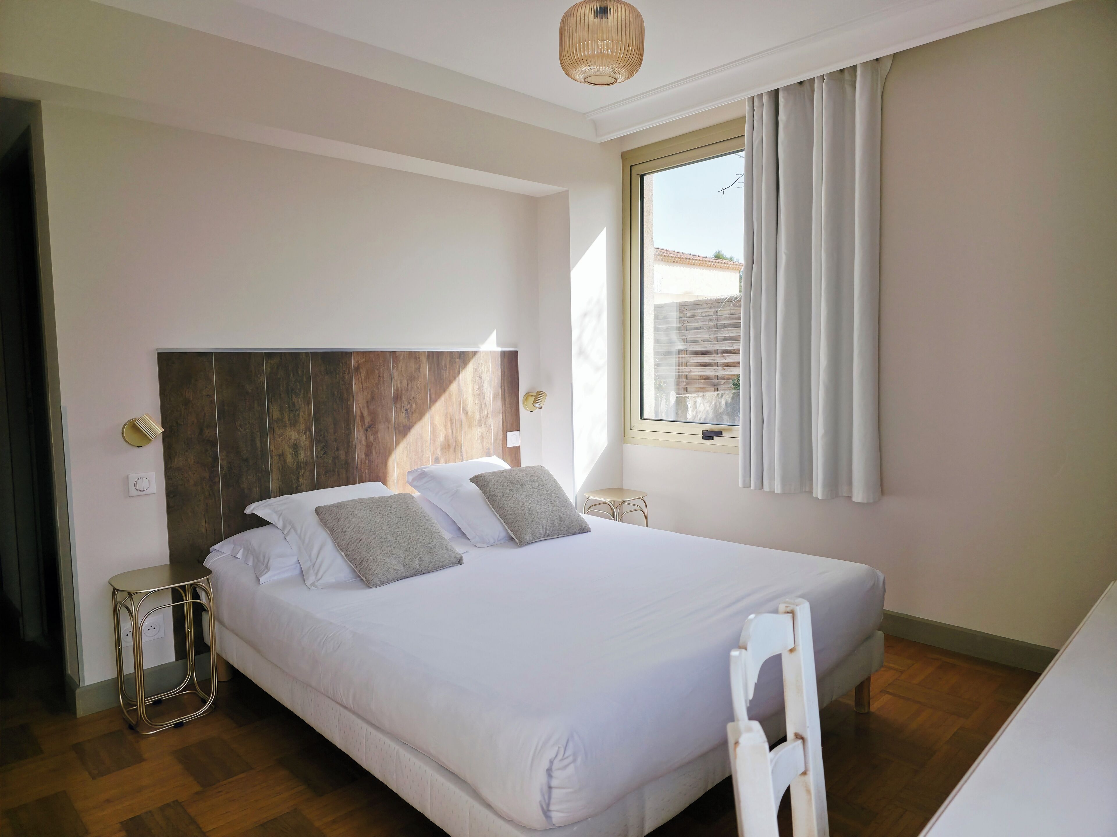Un dormitorio con una cama grande, una mesita de noche, cortinas en la ventana y una lámpara de techo.